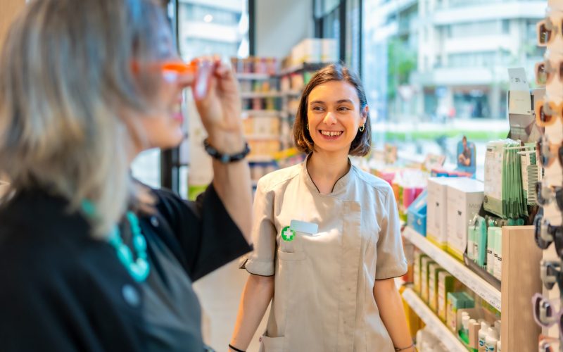 Ophthalmologist smiling while a client is trying on new glasses Young happy female ophthalmologist smiles and approves the glasses that a client is trying on